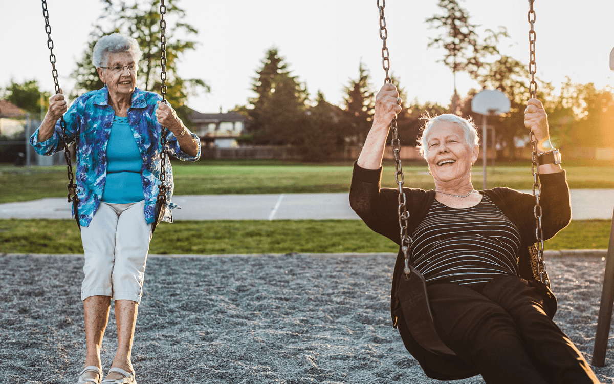 Two senior ladies swinging on a swingset.